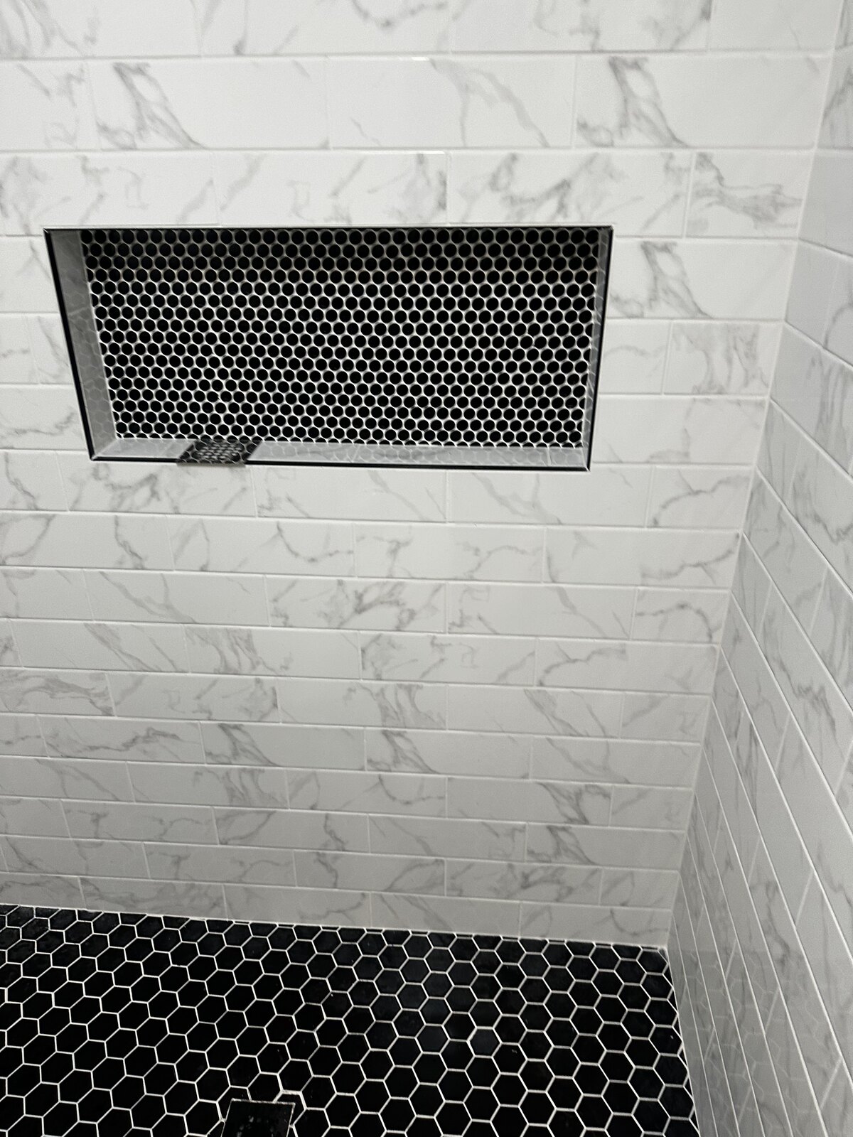 Marble subway tile shower with black hexagon niche and glass enclosure