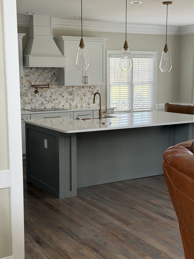 Renovated kitchen with gray island, white cabinets, gold-and-white mosaic backsplash and glass pendant lights