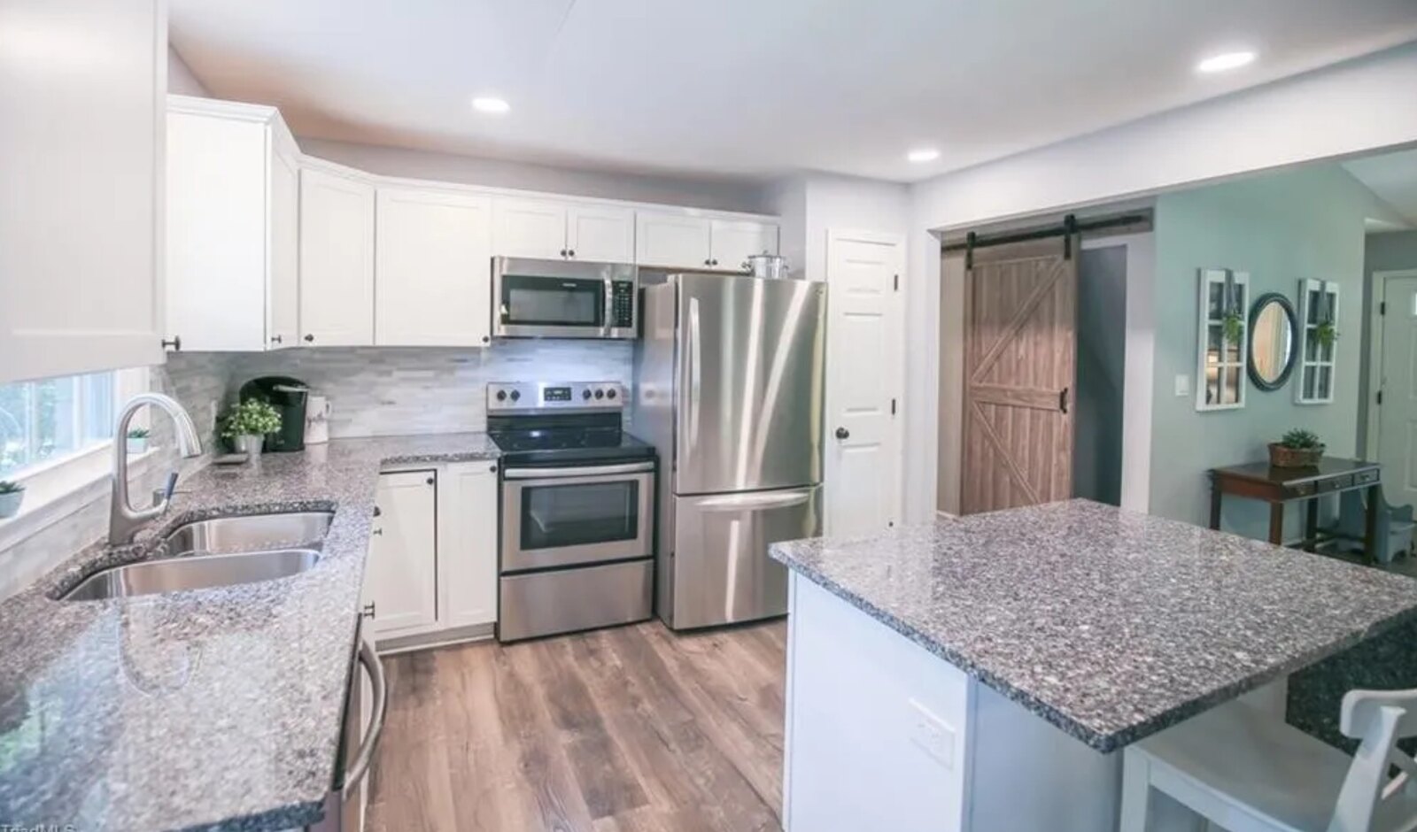 Modern kitchen with white cabinets, stainless steel appliances, granite countertops and sliding barn door