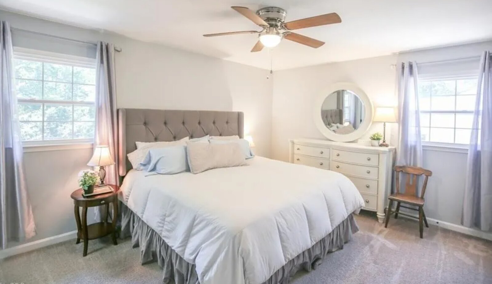 Master bedroom with upholstered tufted headboard, round mirror and ceiling fan