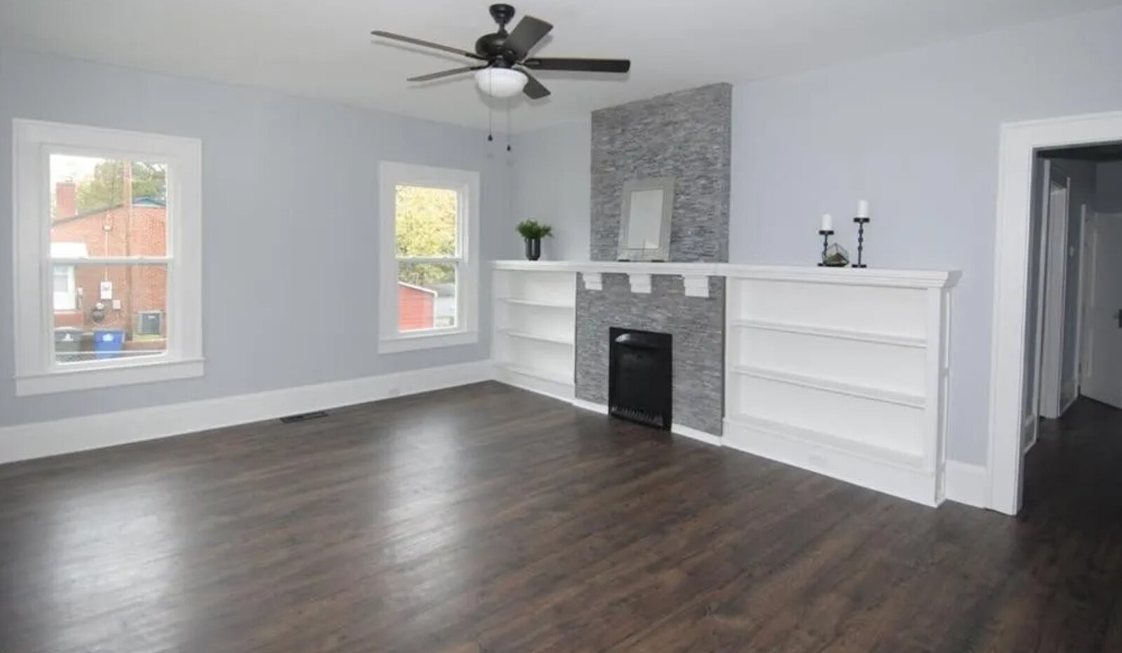 Living room with stacked stone fireplace, built-in shelving and dark LVP flooring