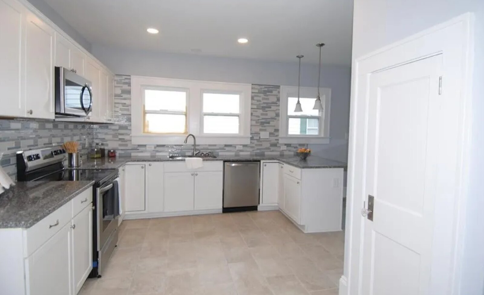 Bright kitchen with white cabinets, tile backsplash, stainless appliances and granite counters
