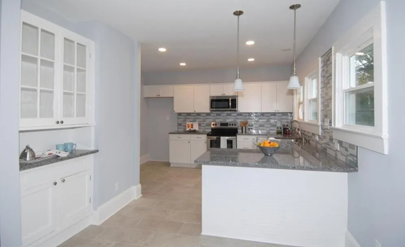 Renovated kitchen with white cabinets, granite peninsula and pendant lighting